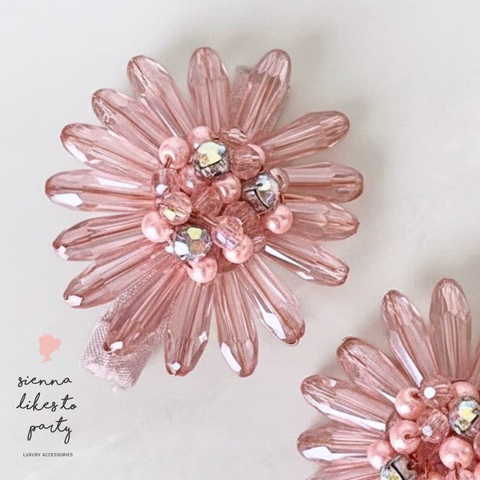 A close-up of a pink faceted crystal flower-shaped brooch with pink beads and clear rhinestones, shown on a light background with part of a second matching brooch visible at the lower right.