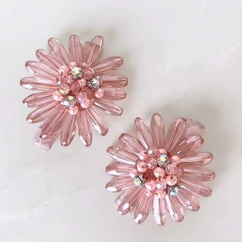 A pair of pink flower-shaped hair clips made from faceted beads and small iridescent rhinestones, displayed on a light off-white background.