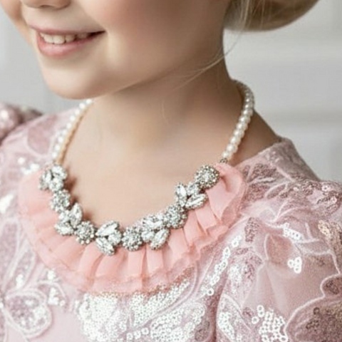 Model wearing Handmade girls rhinestone and blush chiffon statement necklace.  A bespoke piece on quality pearl beads.  Fully adjustable clasp.  Created by Sienna Likes to Party, luxury accessories for children.  Worldwide shipping